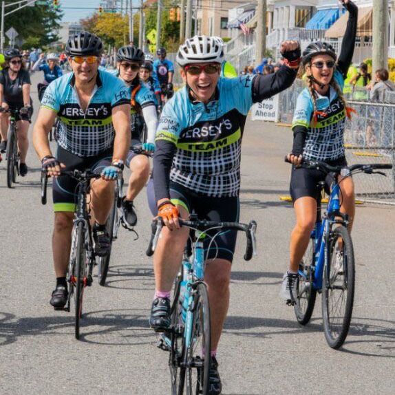 Kevin Moffitt riding a bike through the finish line of a Bike MS event while throwing his fist in the air with joy.